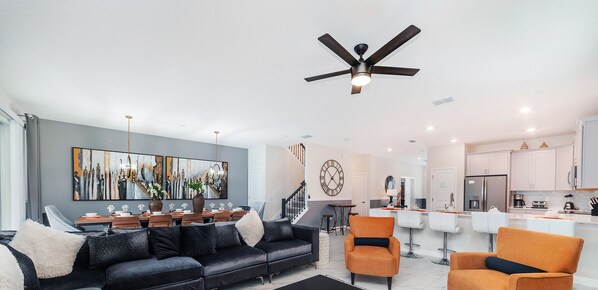 A modern living room with a black sofa, orange chairs, a dining area, and a kitchen in the background. - Special Offer! Walk to Target, Private pool and SPA, Storey Lake 4549 (Kissimmee)
