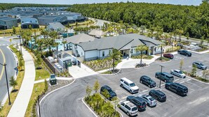 Suuri parkkipaikka, jossa on useita autoja, harmaakattoinen rakennus ja tie, joka kaartuu parkkipaikan ympäri.
