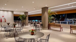 A spacious indoor area with round tables and chairs, potted plants, and benches. - Rua Projetada A (Olímpia)