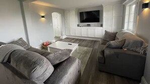 Un salon moderne avec un téléviseur à écran plat fixé sur un meuble blanc, des canapés gris et une table basse blanche.