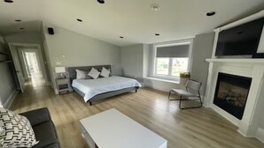 Une chambre spacieuse avec un grand lit, une table de chevet blanche, une chaise, une cheminée et un téléviseur fixé au-dessus.