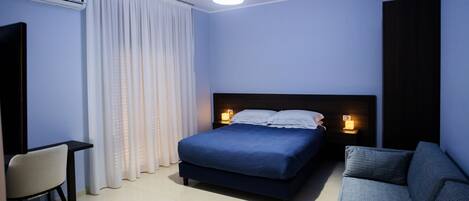 A bedroom with a bed, bedside lamps, a chair, and a sofa.