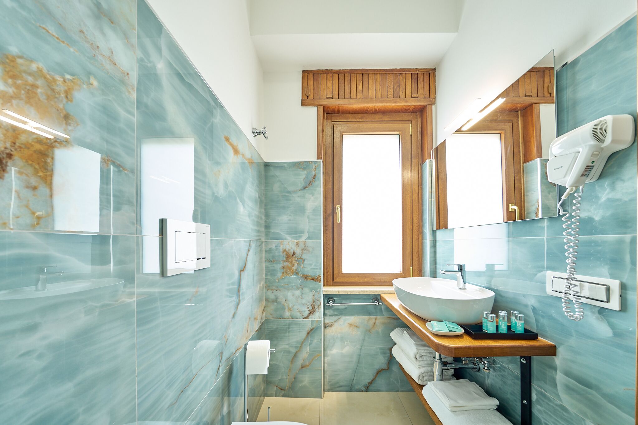A modern bathroom with a large mirror, a round sink, and a hairdryer mounted on the wall.