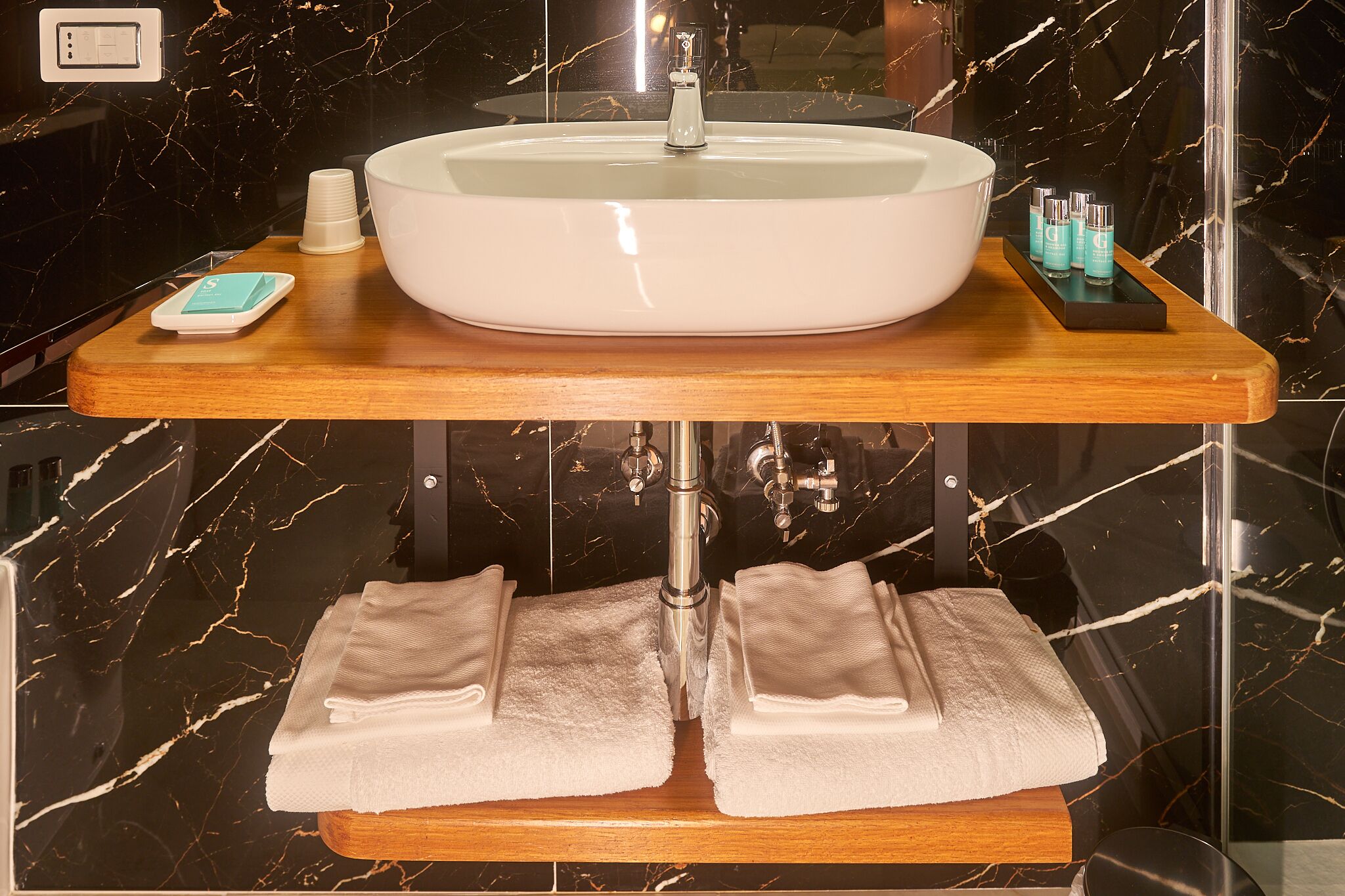 A bathroom with a marble sink, a wooden vanity, and two towels.