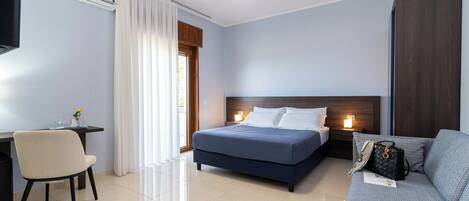 A modern hotel room with a bed, a sofa, a desk, and a chair.