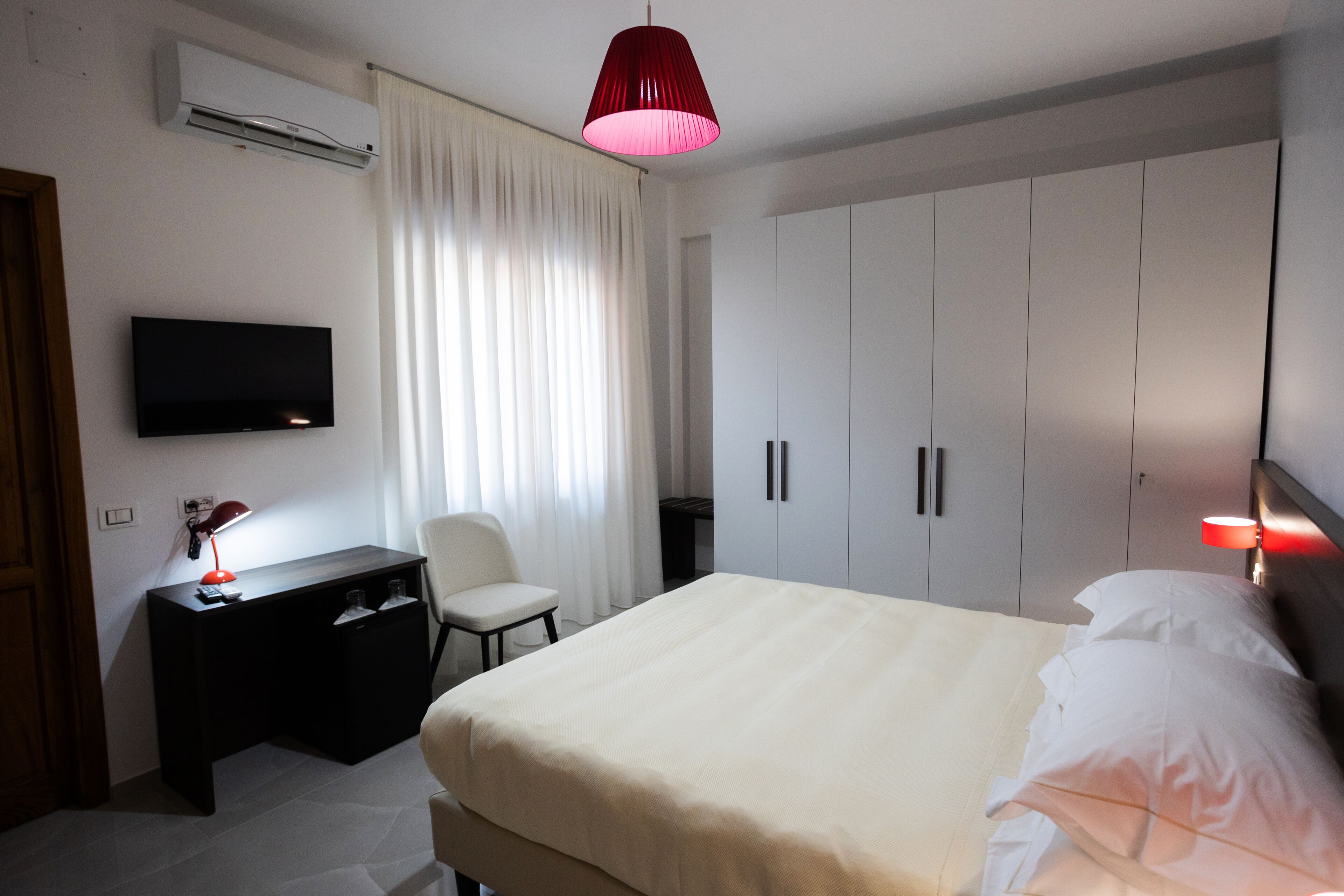 A hotel room with a bed, a desk with a lamp, a TV, and a wardrobe.