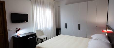 A hotel room with a bed, a desk with a lamp, a TV, and a wardrobe.