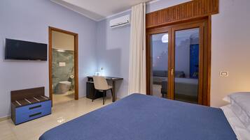 A hotel room with a bed, a desk, a chair, a television, and a sliding glass door leading to an outdoor area.