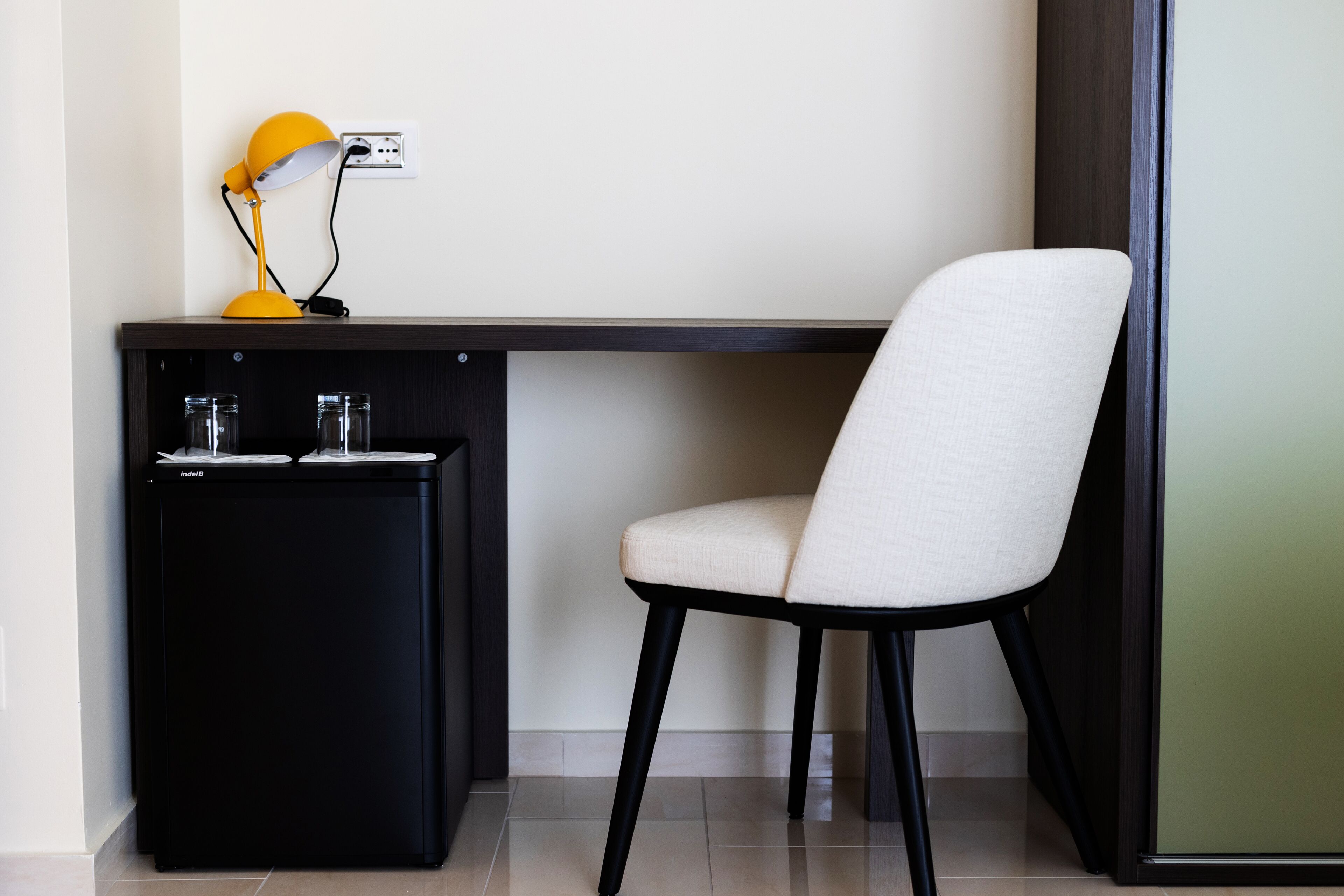 A compact workspace with a desk, a chair, a small black cabinet, and a yellow desk lamp.