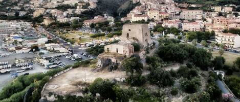 Vista aérea de un pueblo con una imponente torre histórica, una plaza central con coches aparcados y edificios residenciales circundantes.
