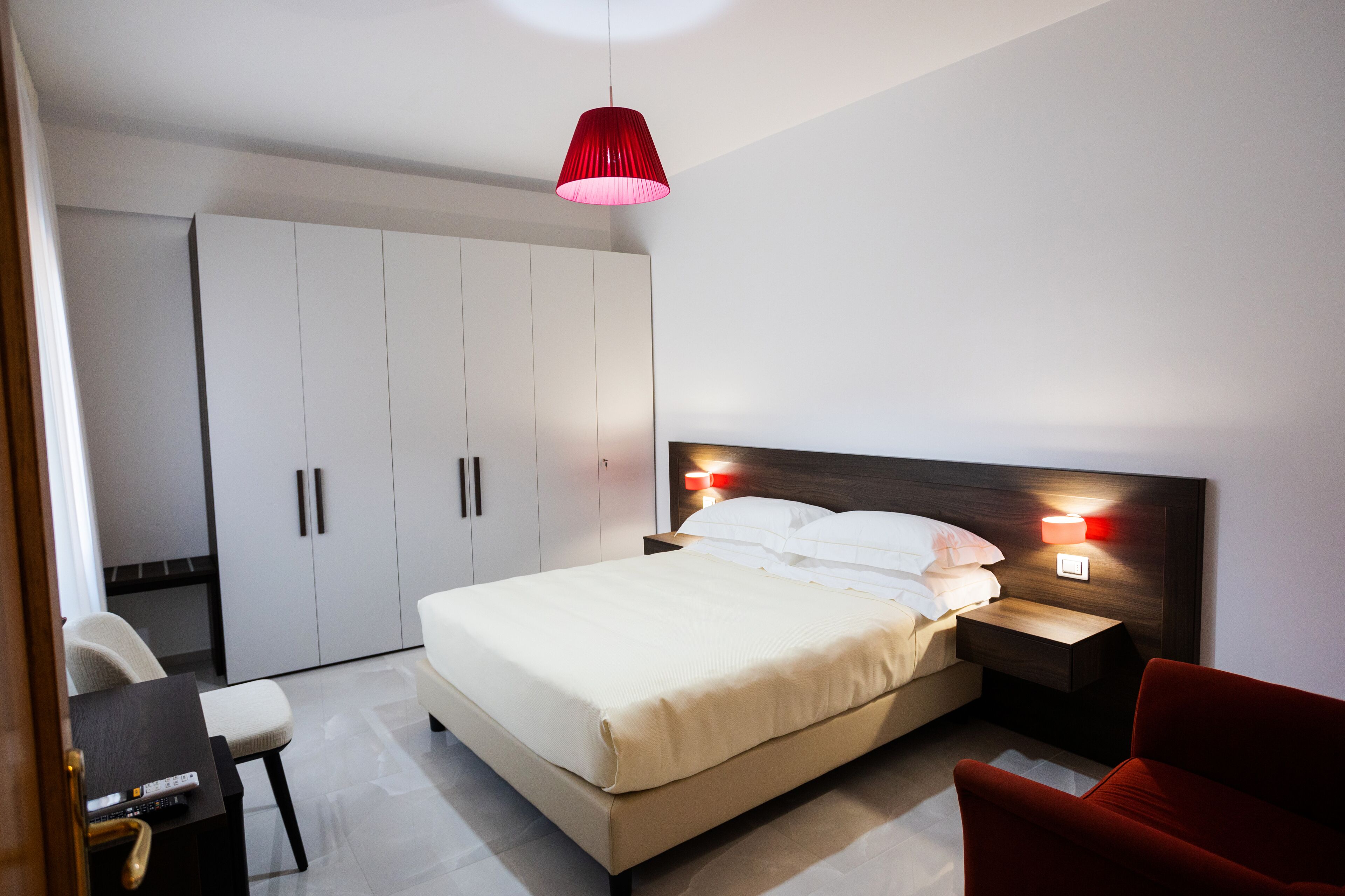 Una camera da letto moderna con un letto grande, una scrivania, una sedia, un armadio e una lampada a sospensione rossa.