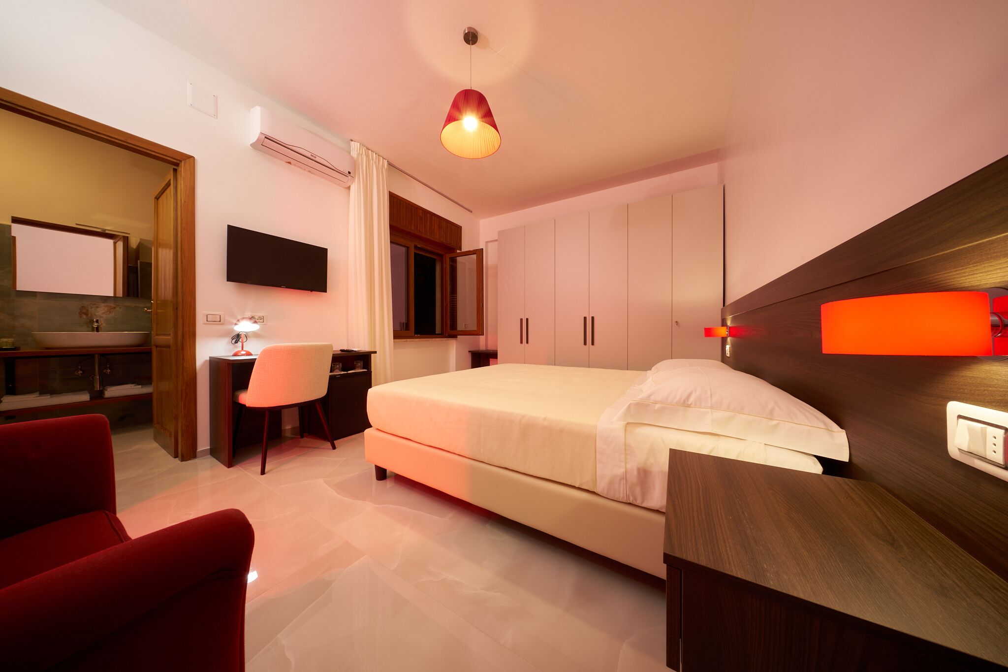 Un dormitorio moderno con una cama, un escritorio, una silla y un televisor fijado a la pared.