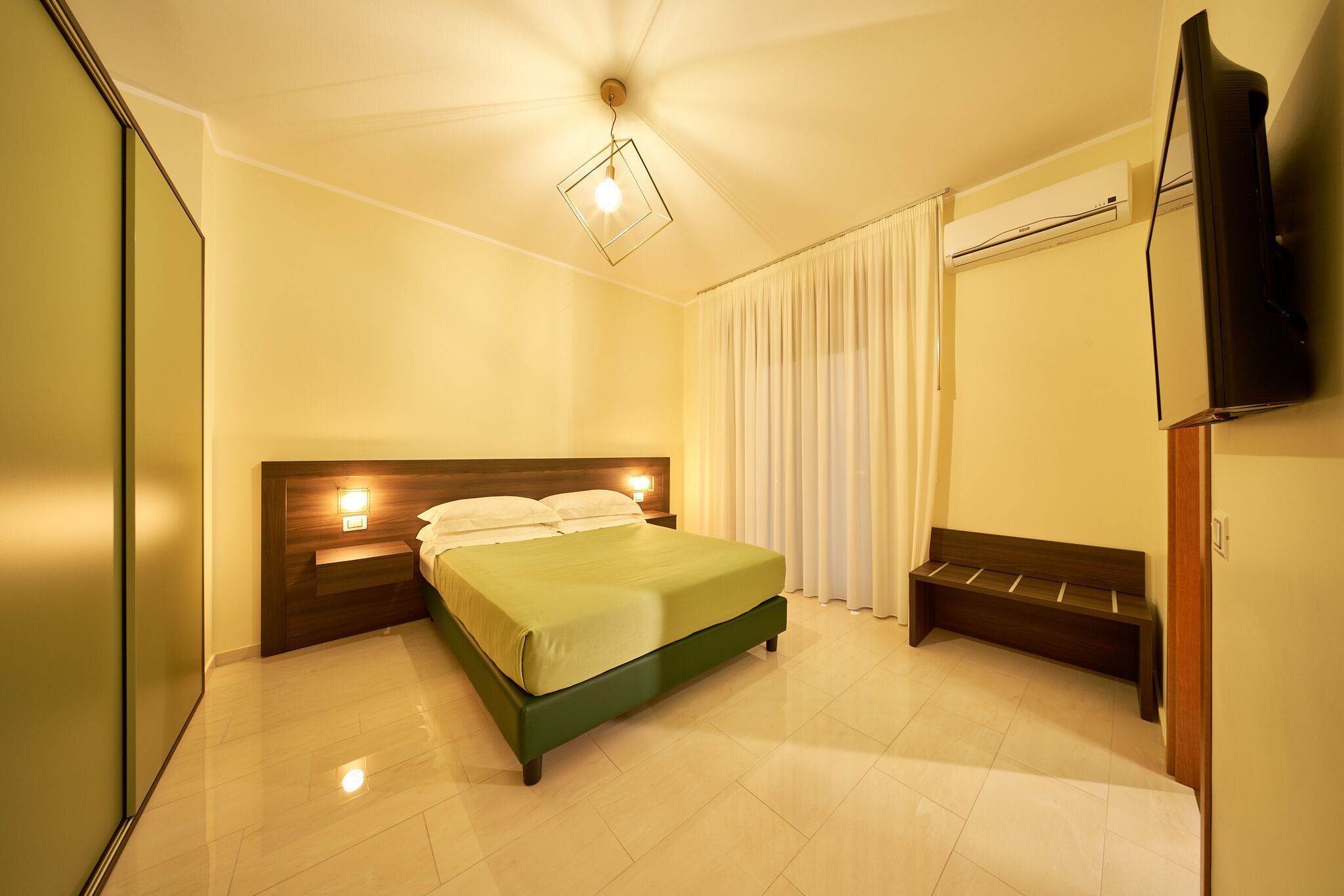 Habitación de hotel con cama, lámparas de noche, un banco, televisión de pantalla plana y equipo de aire acondicionado.