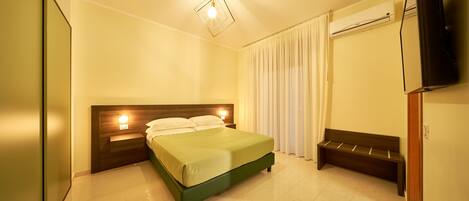 Habitación de hotel con cama, lámparas de noche, un banco, televisión de pantalla plana y equipo de aire acondicionado.