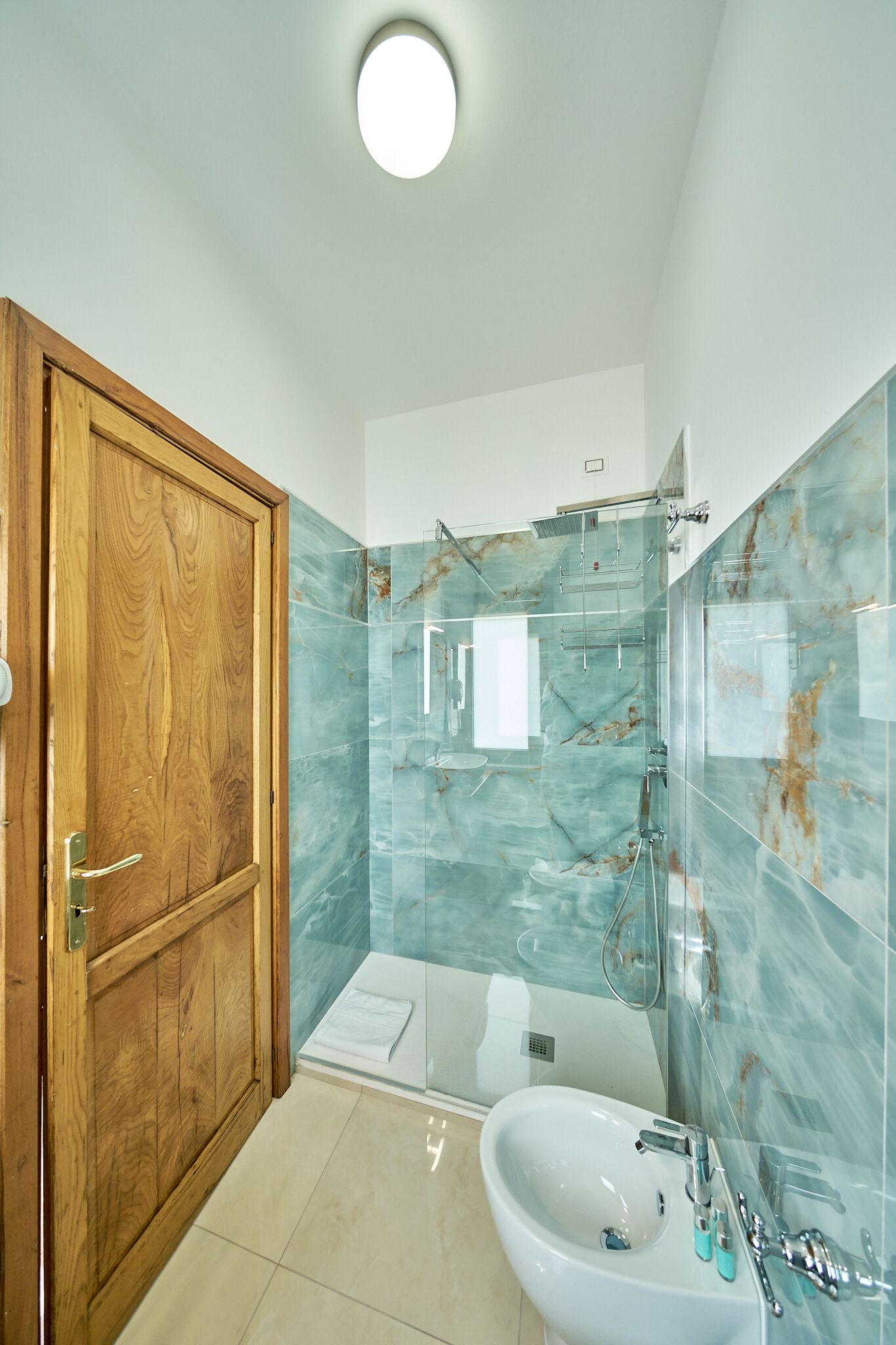 Un bagno moderno con una porta in legno, un box doccia in vetro e un lavandino bianco.