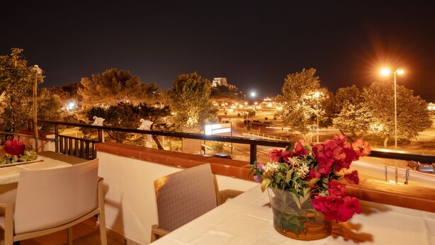 A restaurant with outdoor seating, a view of the city, and a vase of flowers on the table.