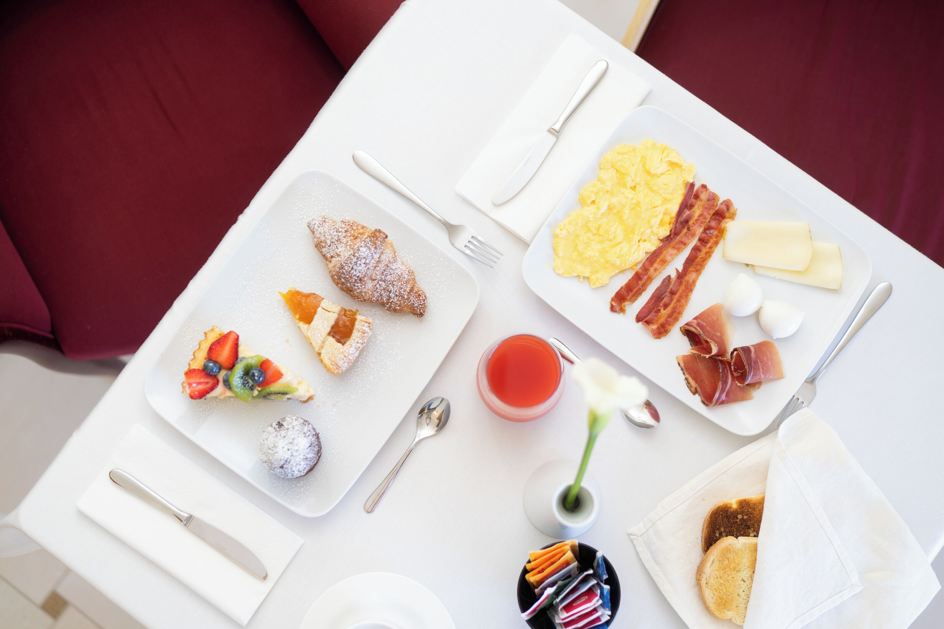 A breakfast table with plates of eggs, bacon, toast, and pastries.