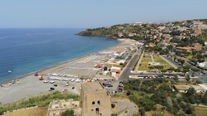 A coastal town with a beach, parked cars, and a historic building. - B&B Torre Talao (Scalea)