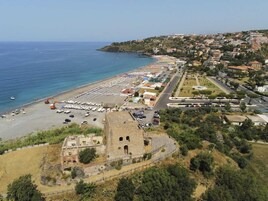 Un pueblo costero con una playa, coches aparcados y un edificio histórico.