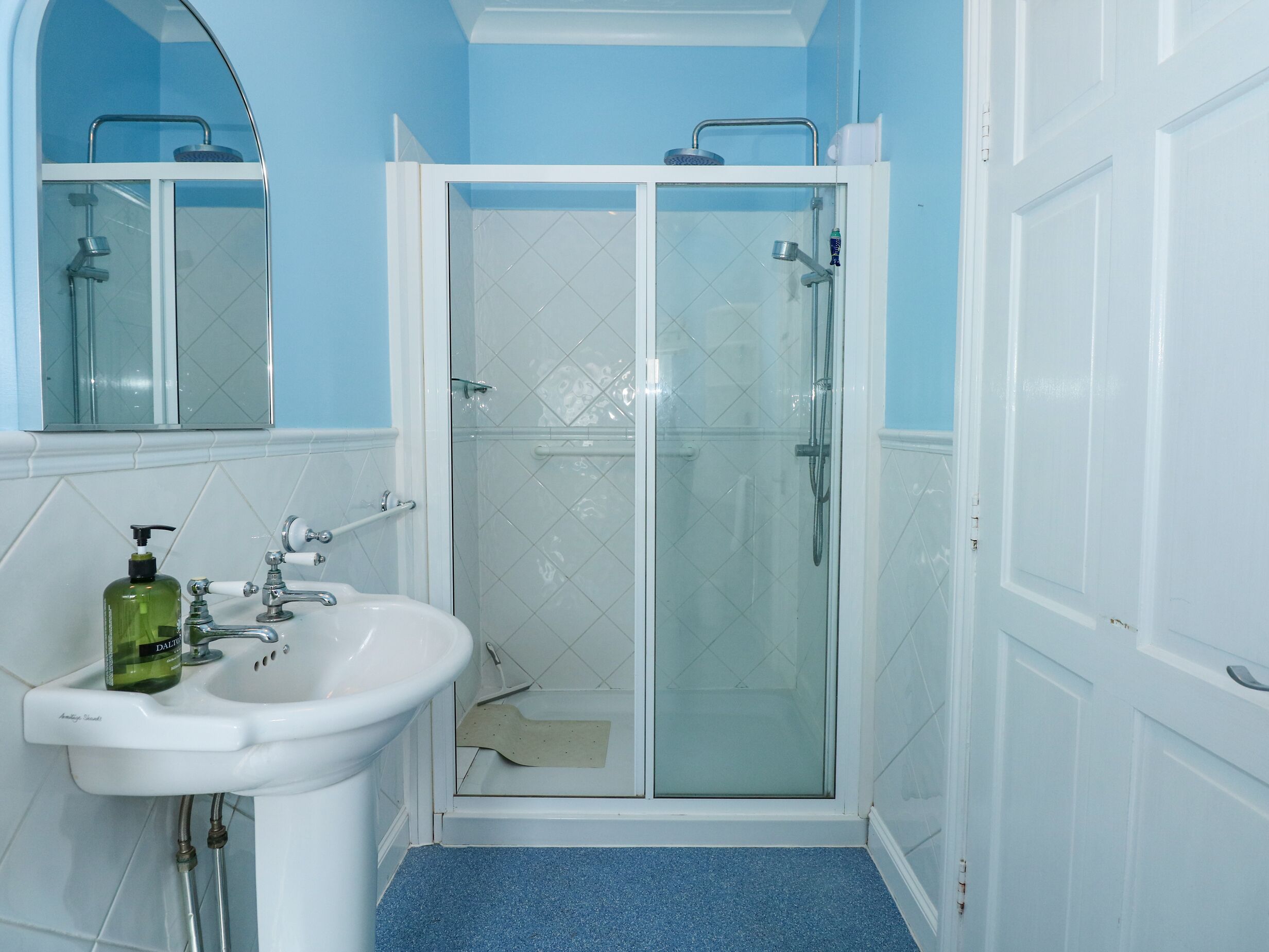 A bathroom with a white sink, a glass shower enclosure, and a blue-tiled floor.
