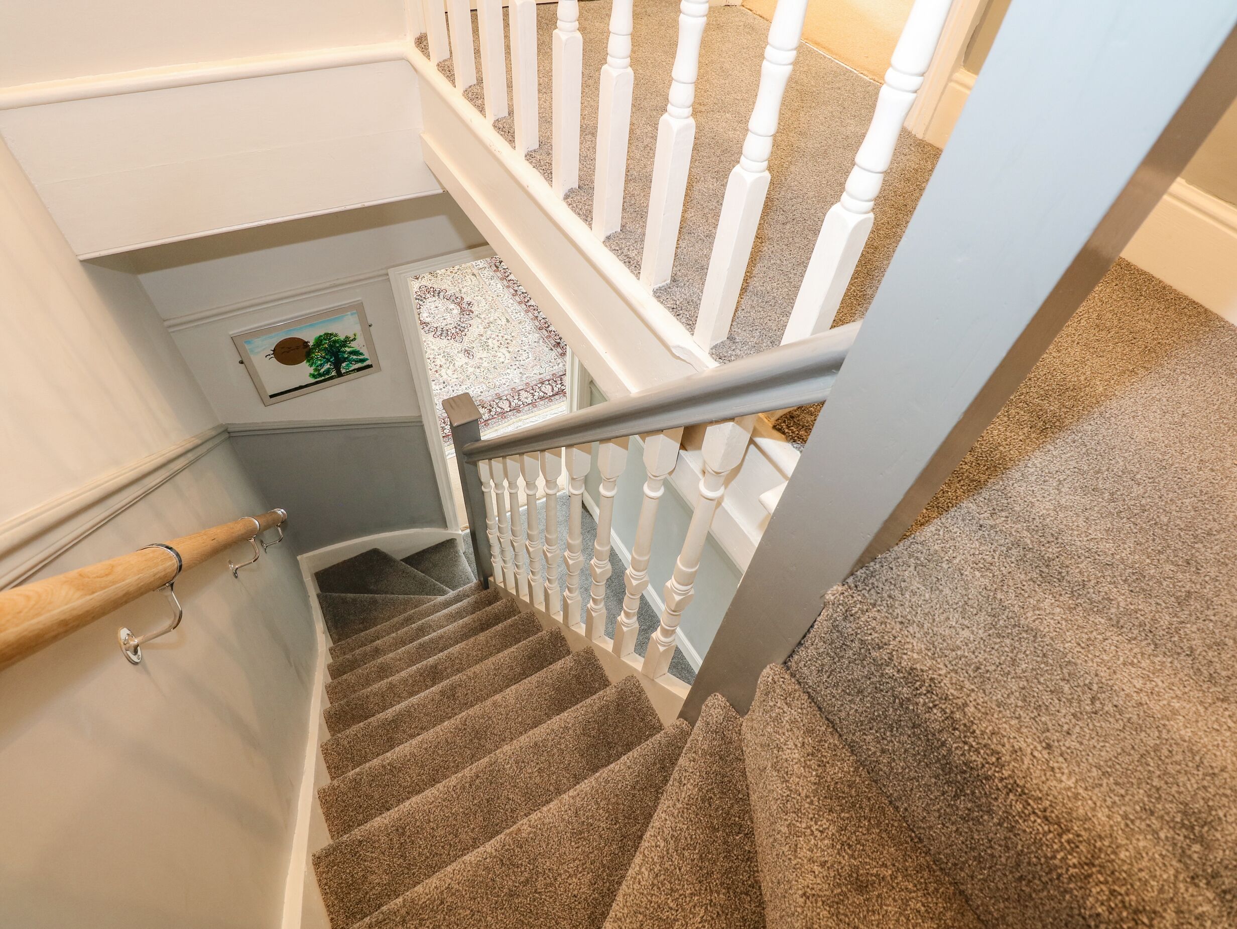 A carpeted staircase with white balusters and a wooden handrail.