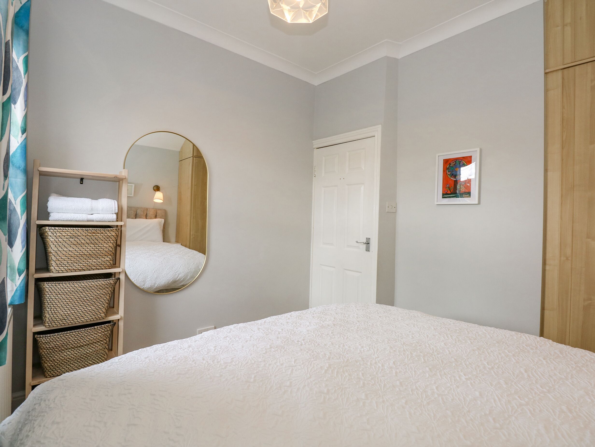 A bedroom with a large bed, a wooden wardrobe, a mirror, and a wall-mounted picture.