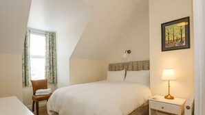 A bedroom with a large bed, a nightstand, a chair, and a window with curtains.