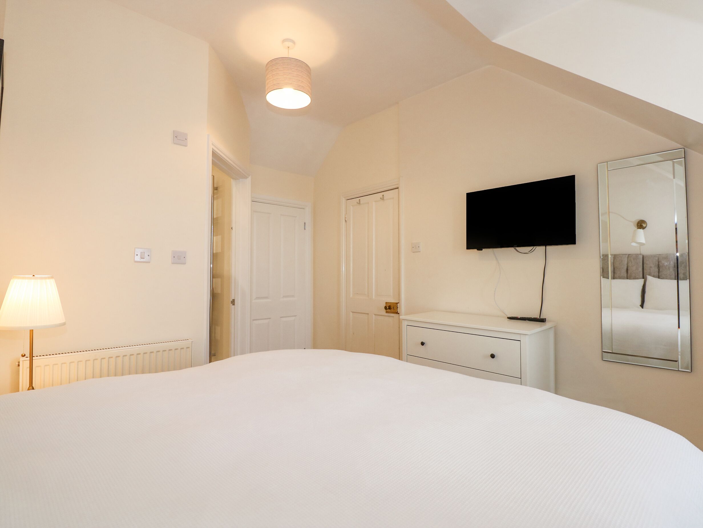 A hotel room with a bed, a dresser, a television mounted on the wall, and a mirror reflecting part of the room.