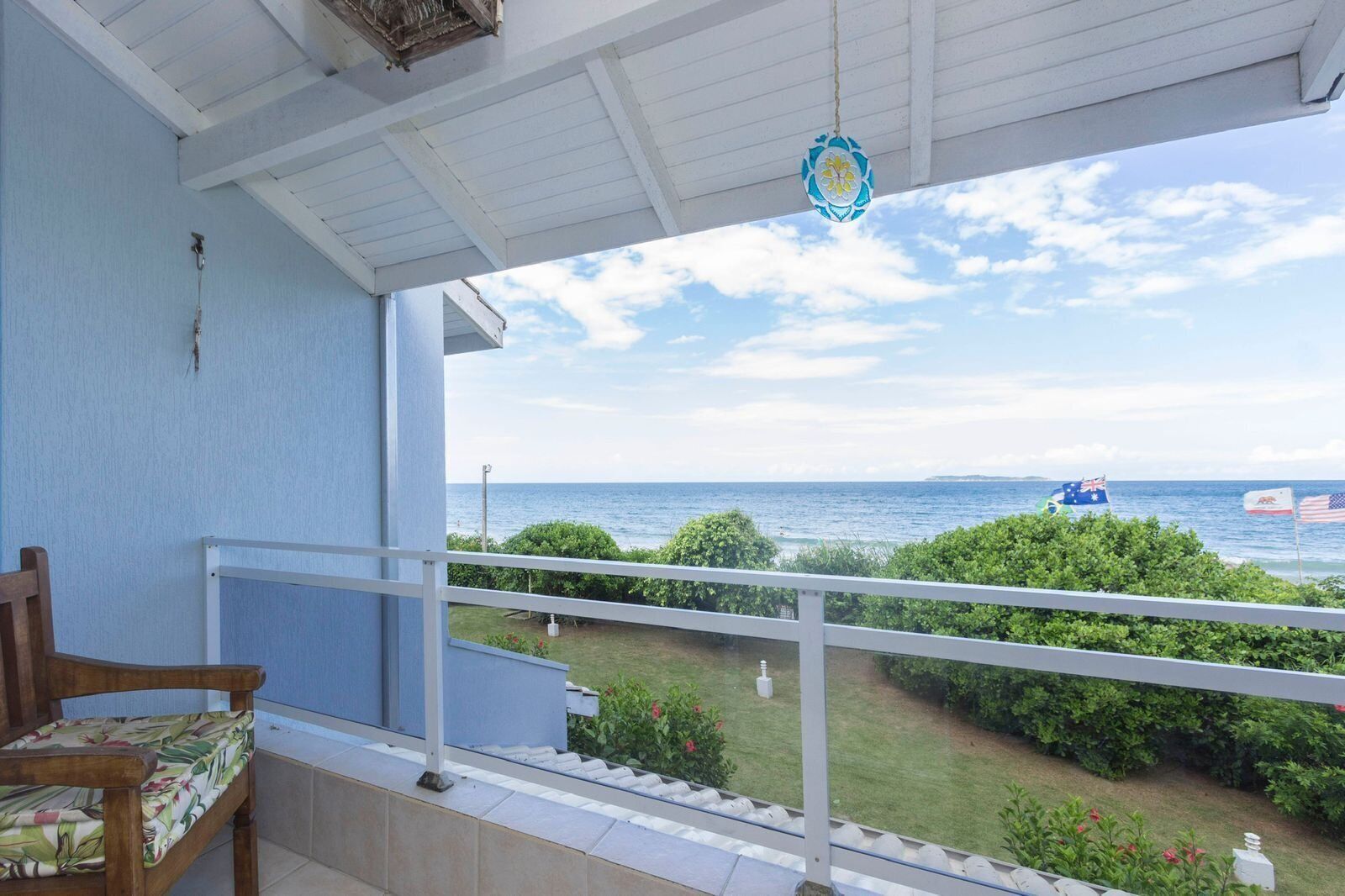 A balcony with a view of the sea, a flag, and a chair.