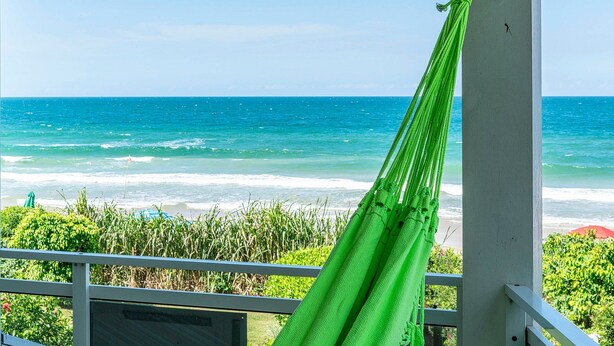 A hammock tied to a balcony railing overlooking a beach with ocean waves. - Residencial Guilhermina (Bombinhas)