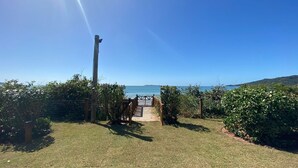A wooden deck leading to a gate with a view of the sea and hills in the background. - Residencial Guilhermina (Bombinhas)