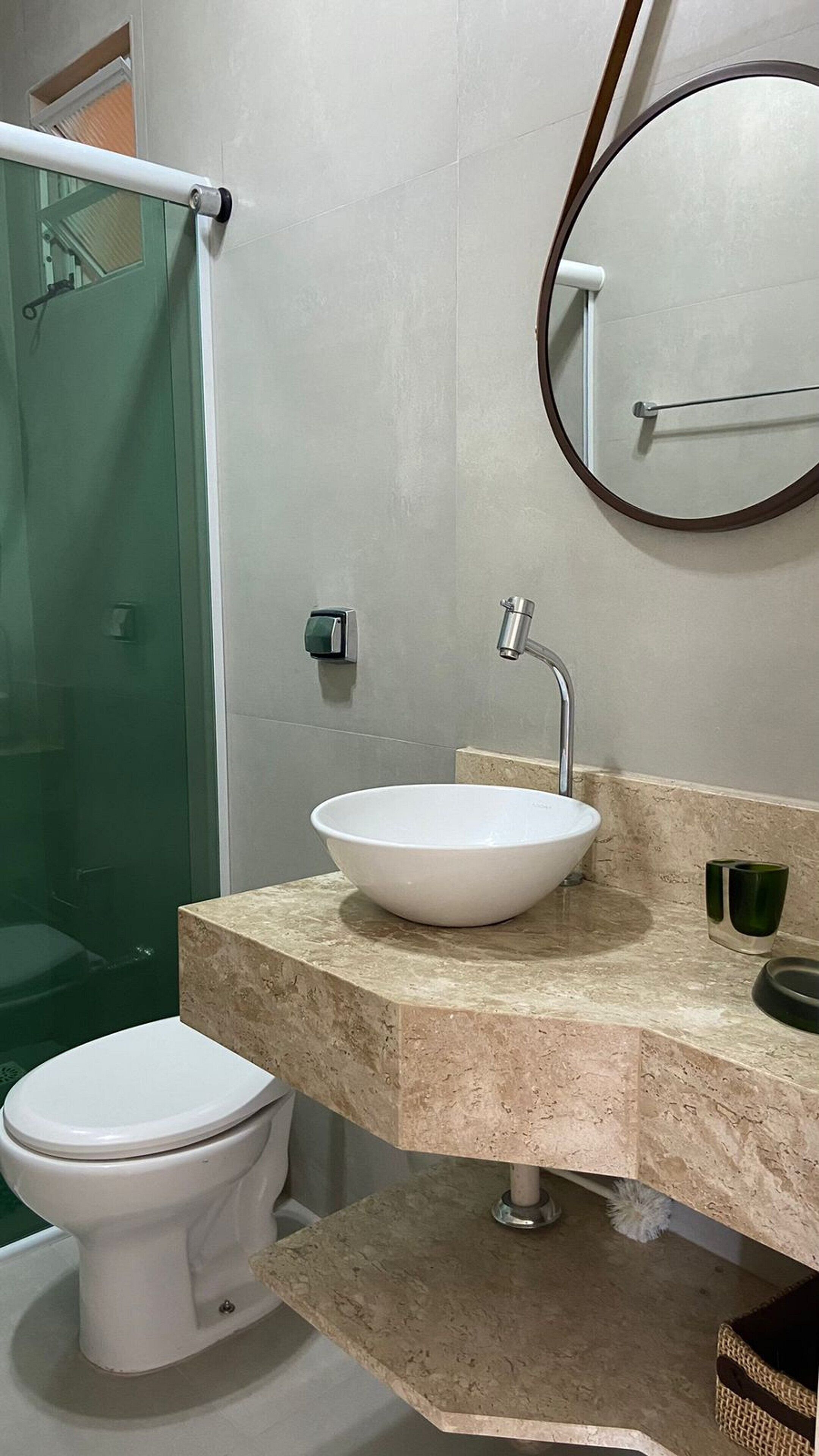 A bathroom with a white toilet, a round mirror, a sink with a marble countertop, and a shower area.