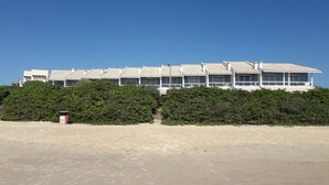 A beachfront hotel with a row of rooms, a sandy beach in the foreground, and dense greenery in the background. - Residencial Guilhermina (Bombinhas)