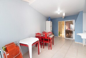 A dining area with a white table and red chairs, a white cabinet, and a blue water dispenser. - Residencial Guilhermina (Bombinhas)
