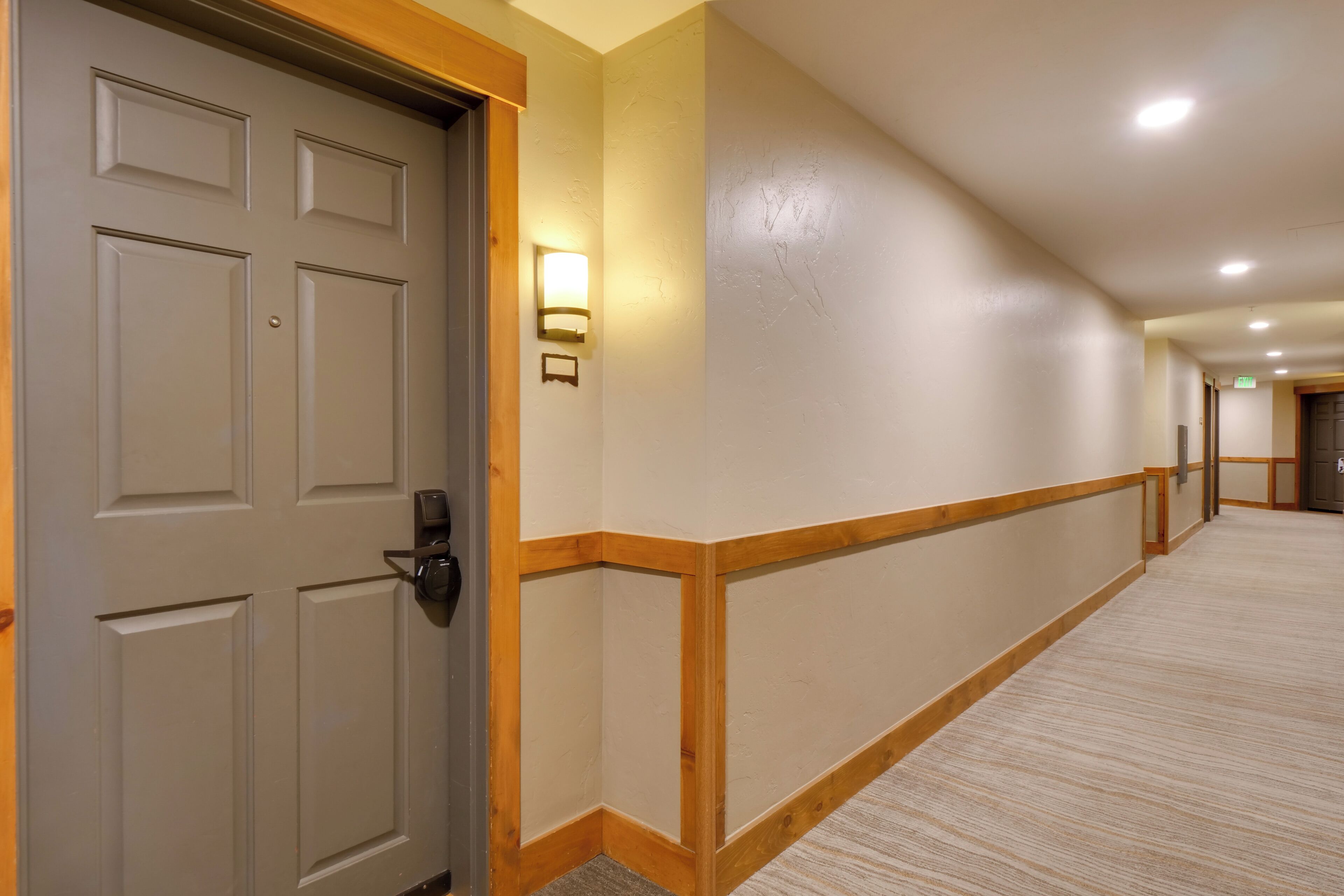Een hotelgang met een houten vloer, een beige muur en een deur met sleutelslot.