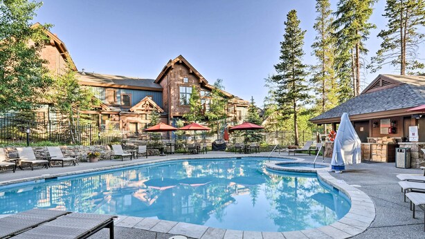 A pool area with lounge chairs, umbrellas, and a building with a stone facade. - Ski-In Breckenridge Condo w/ Fireplace + Balcony! (Breckenridge)
