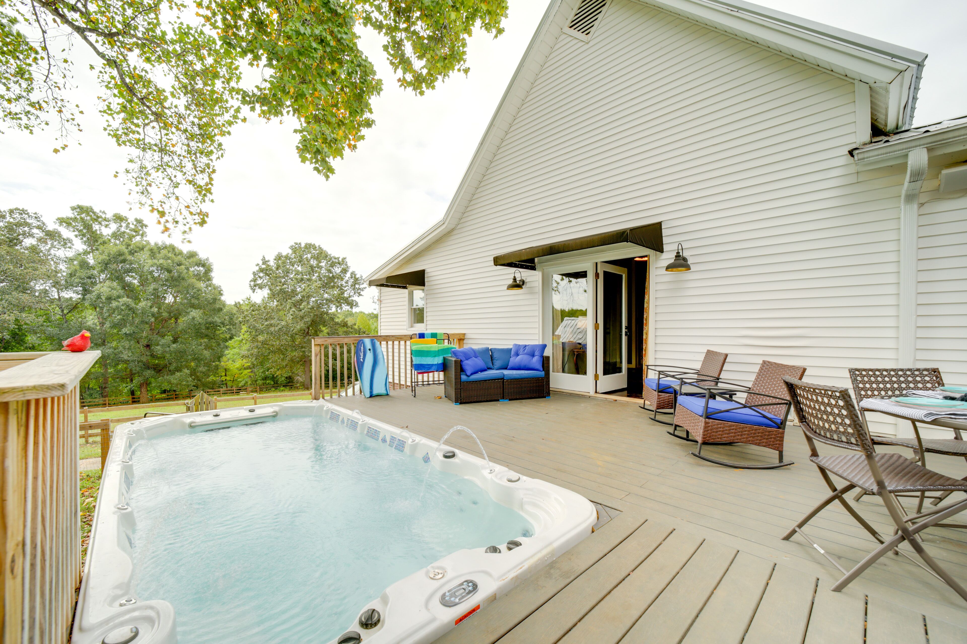 A hot tub on a wooden deck with outdoor furniture and a white building in the background.