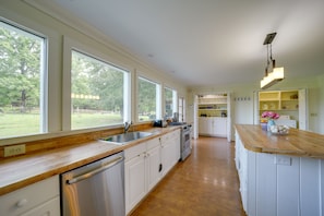 A kitchen with a wooden countertop, stainless steel appliances, and a view of a green landscape through large windows.