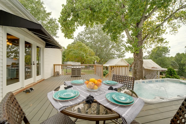 A deck with a glass-top table set for dining, surrounded by a swimming pool and a barbecue grill.
