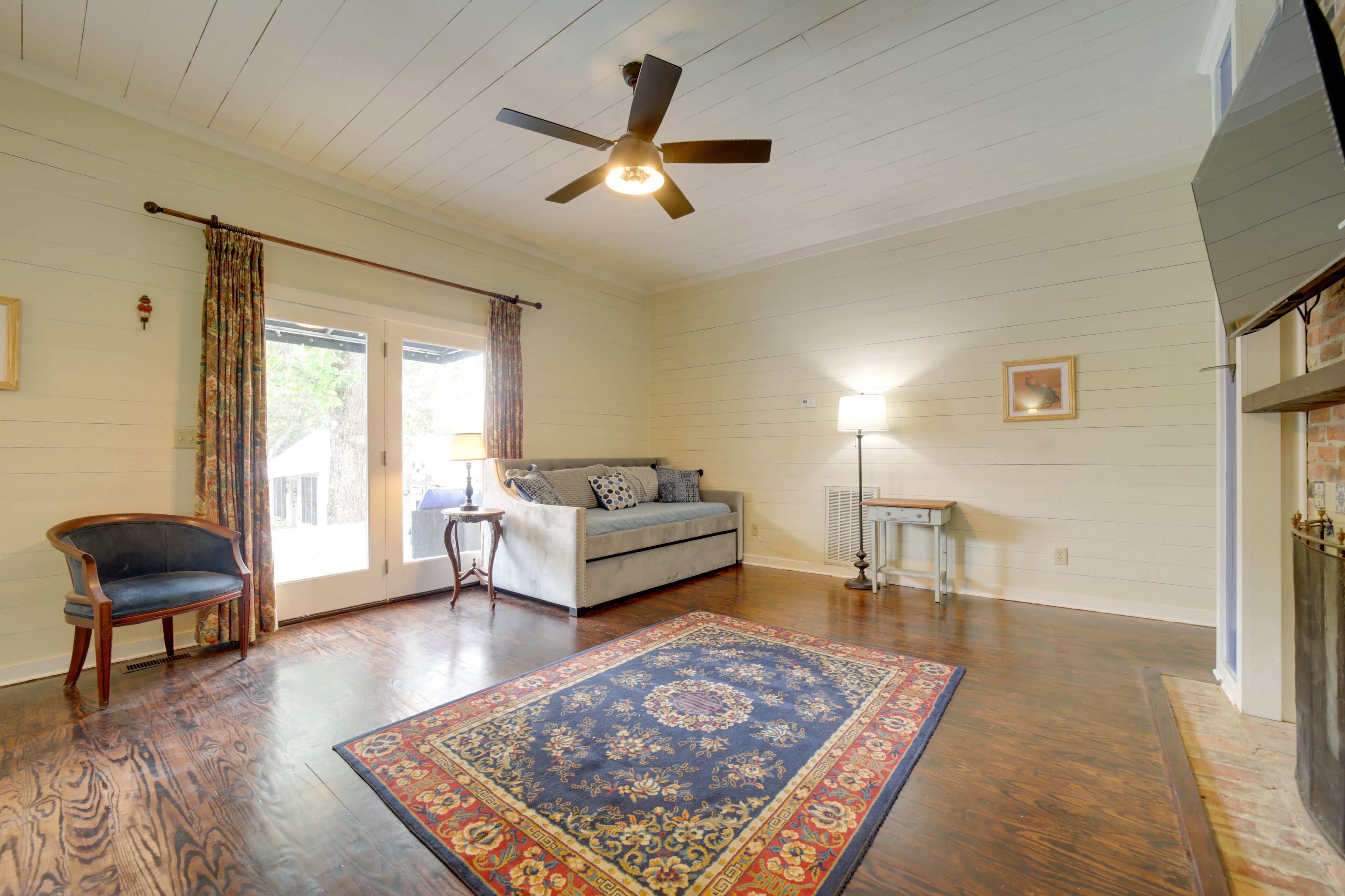 A room with a ceiling fan, a sofa, a chair, a rug, and a lamp.