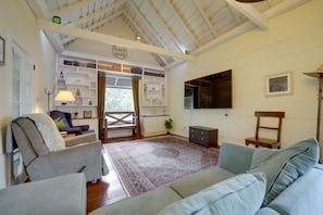 A cozy living room with a high ceiling, built-in bookshelves, a large window with curtains, and a flat-screen TV mounted on the wall.
