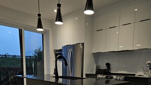 Una cocina moderna con una isla central, taburetes de bar, electrodomésticos de acero inoxidable e iluminación colgante.