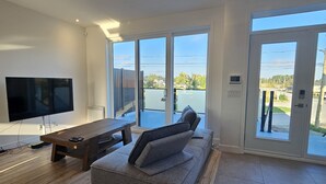 Una sala de estar moderna con un televisor de pantalla plana grande, una mesa de centro de madera y un sofá gris.
