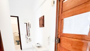 A hallway with a wooden door, white walls, and a tiled floor. - T1 Largo Frente - Familiar (Loulé)