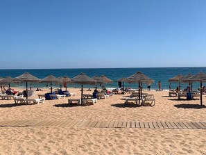 Una playa con tumbonas y sombrillas de paja.