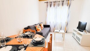 A dining area with a round table, chairs, and a sofa in the background. - T1 Largo Frente - Familiar (Loulé)