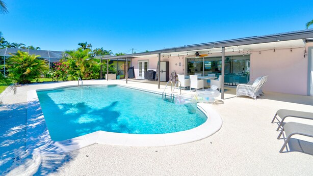 Une piscine dotée d’un espace salon en contrebas, entourée de palmiers et agrémentée d’une terrasse couverte avec des meubles d’extérieur.