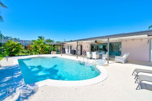 Une piscine dotée d’un espace salon en contrebas, entourée de palmiers et agrémentée d’une terrasse couverte avec des meubles d’extérieur.