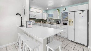 Une cuisine moderne avec des meubles blancs, un îlot central doté de tabourets, un réfrigérateur et un four à micro-ondes.