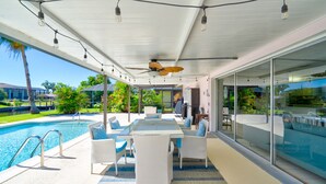 Une terrasse extérieure avec une piscine, des meubles en osier blancs et un ventilateur de plafond.